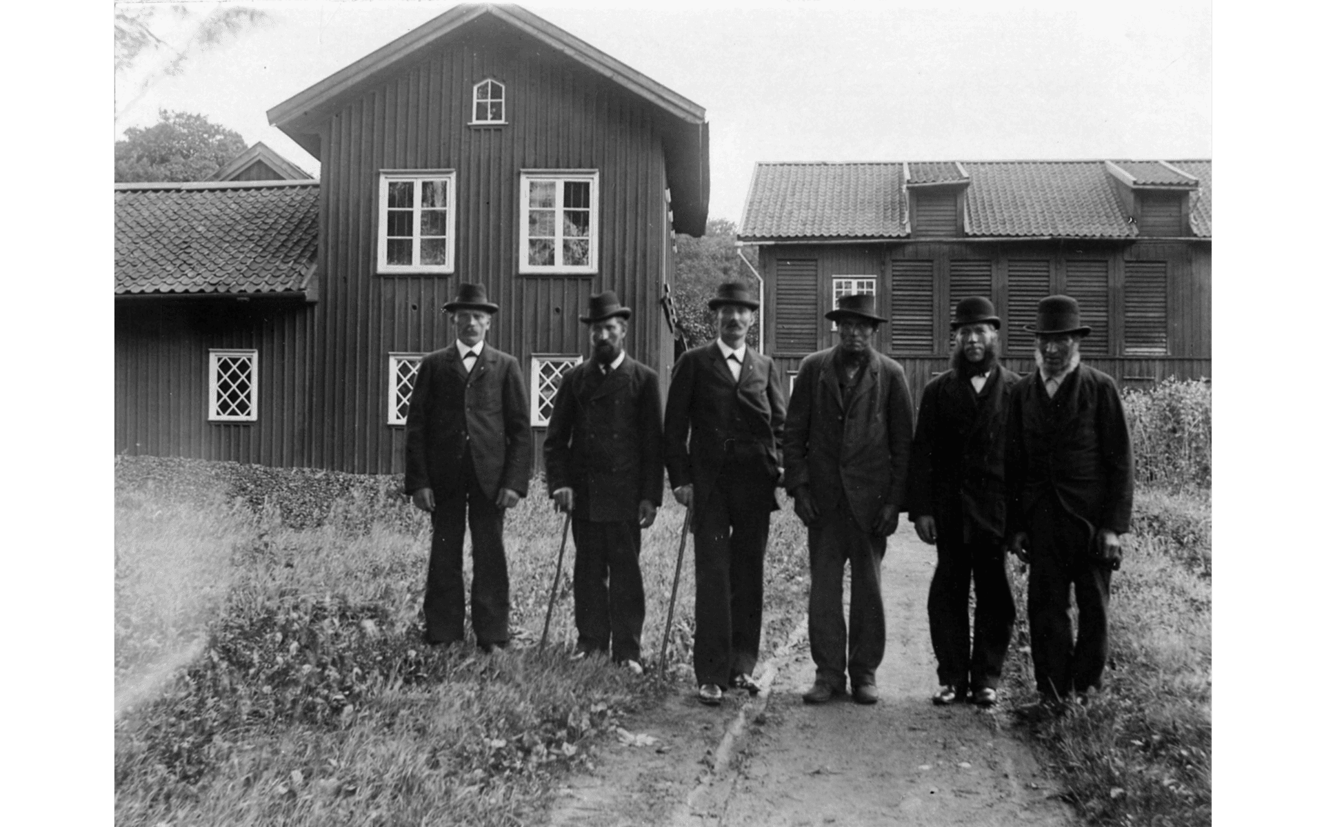 Gruppbild på 6 garveriarbetande män, uppställda på rad framför Brunos Garver i kv. Hjulet vid Lugnet. Fotografering - 1875-1900