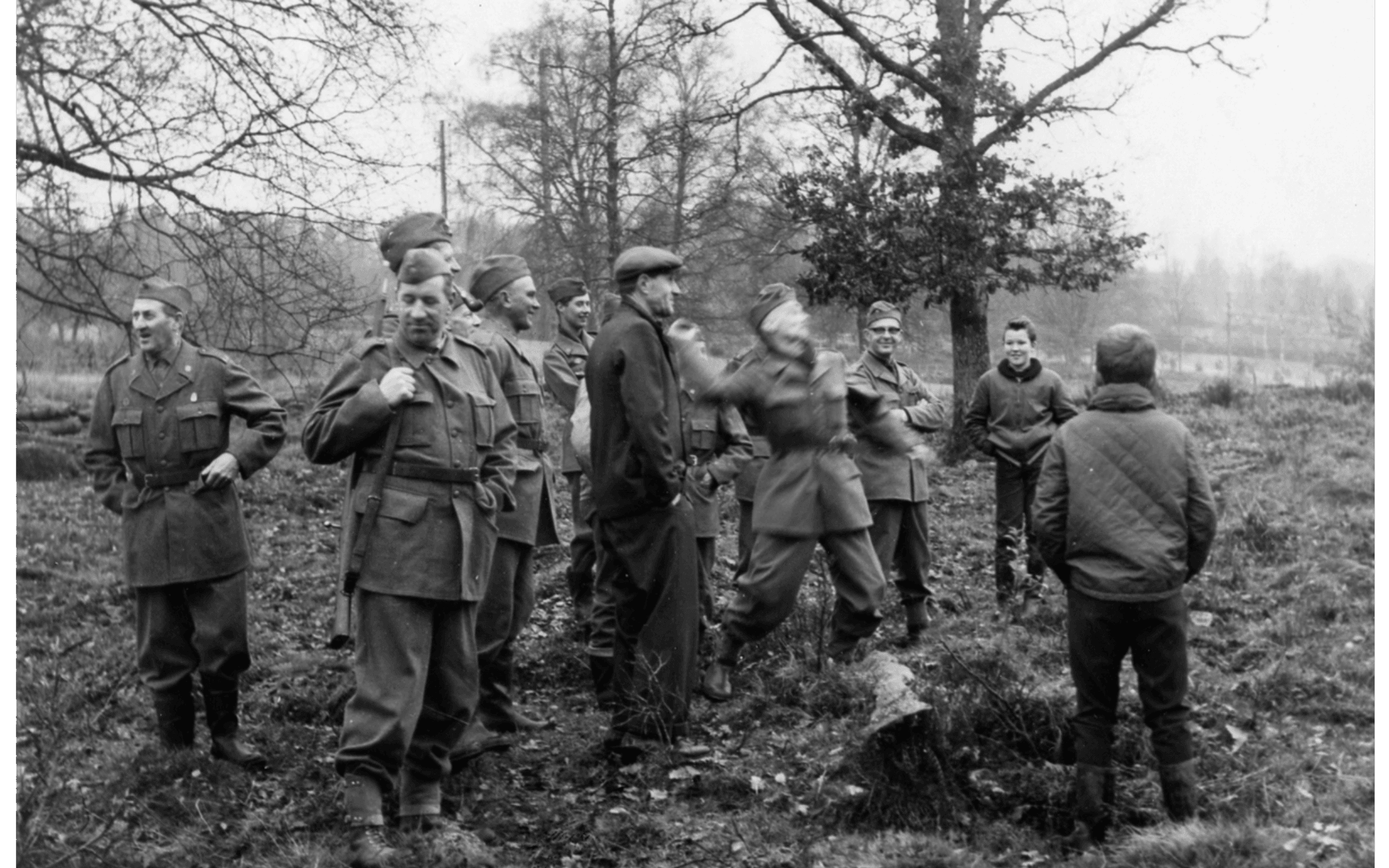 Hemvärnsövning, Fjorton personer i skogen: elva män i sina uniformer, en civilklädd man och två civilklädda pojkar. Fotografering - 1960-talet.