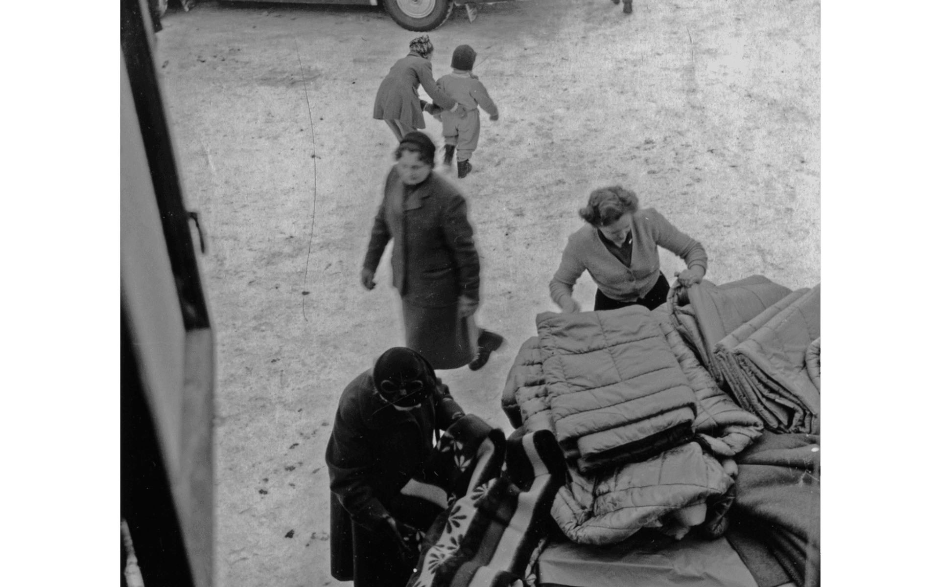 Vy från fönster uppifrån, tittar ned mot ett 3 kvinnor som inspekterar filtar och madrasser på auktion på gården till Tells hus. En bil syns i bakgrunden. Kvarteret Jägaren 11. Kungsgatan 38. Fotografering - 1950-tal.