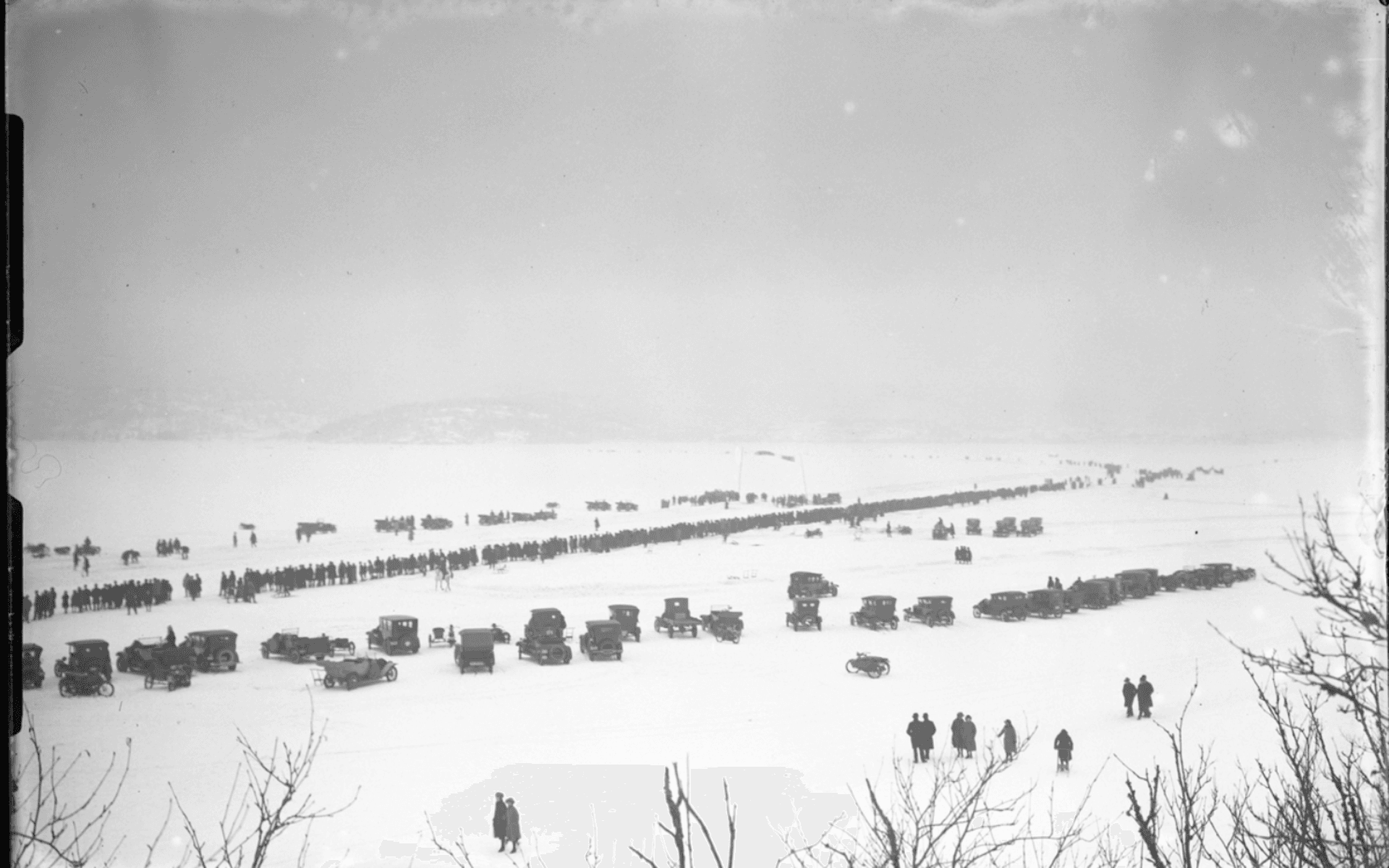 Bilar och åskådare ute på isen på Mjörn i samband med motortävling. Fotografering - 9 mars 1924.